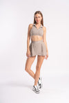 Beige athletic set with a sleeveless collared crop top and pleated skirt, designed for fitness