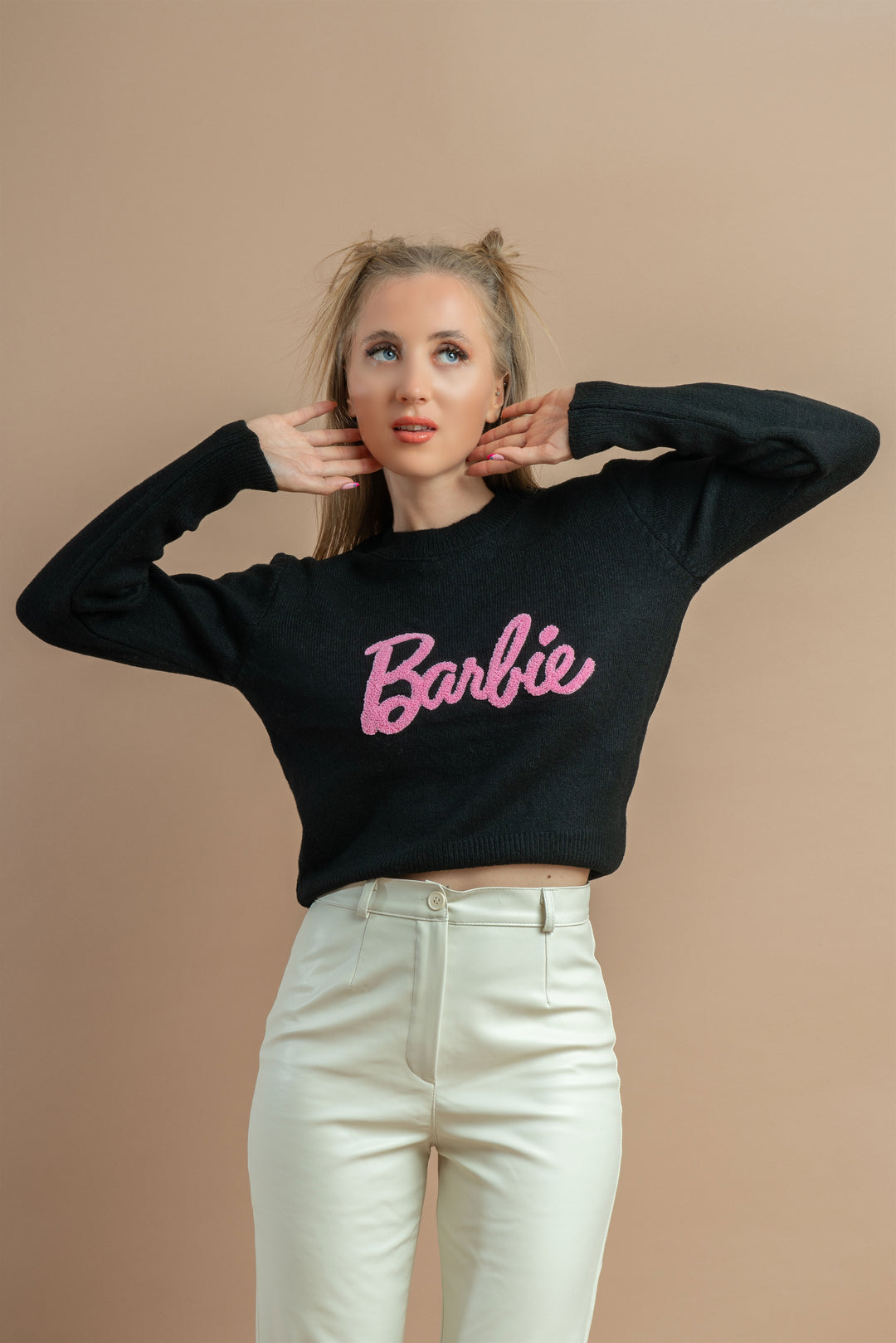 Woman wearing a black sweatshirt with pink 'Barbie' embroidery, paired with high-waisted white pants