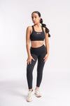 Model in a stylish black yoga outfit, including leggings and a sports bra, standing in a yoga pose.