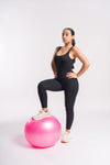 A woman in a black leotard gracefully poses with a pink exercise ball