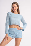 Woman in a light blue crocheted crop top and shorts, posing confidently