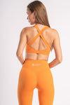 Model dressed in bright orange yoga pants and a coordinating sports bra, ready for a workout.