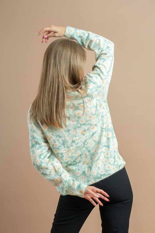 Blonde woman wearing a light green floral sweater and black trousers