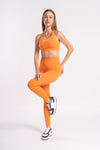 Woman wearing an orange sports bra and matching yoga pants, posing in a fitness stance