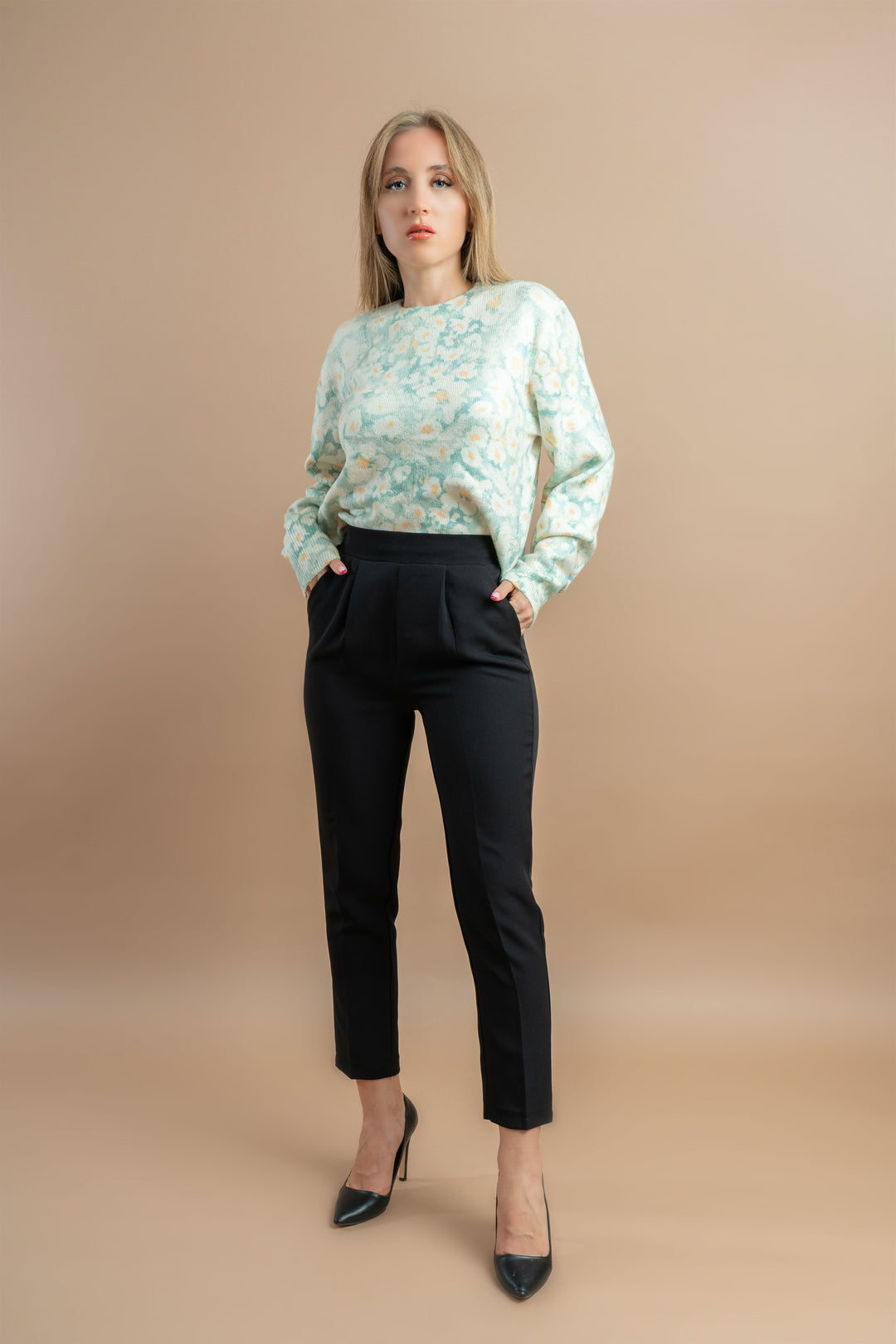 woman in a pastel floral knit sweater paired with black pants, posing with a neutral expression