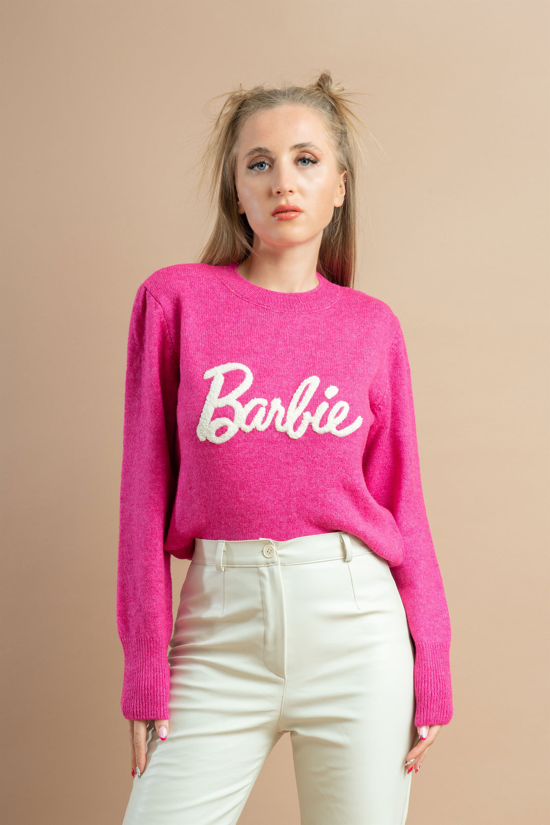 Woman wearing a bright pink sweatshirt with a white Barbie logo paired with off-white high-waisted pants