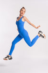 woman showing a jumping pose wearing a blue color jumpsuit unitard for gym and workout