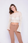 Woman smiling in a cream crochet crop top with bell sleeves, paired with brown pants.