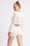 Back view of a woman in a white crochet outfit, featuring a cropped long-sleeve top and shorts