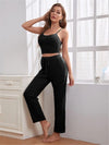 A relaxed woman in a black lounge set, featuring a cropped spaghetti strap top and drawstring pants,