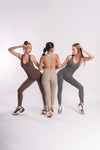 Three woman posing together in full length jumpsuits of beige, grey and brown color ready for gym day