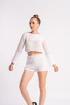 woman wearing a white crochet crop top and shorts, standing confidently